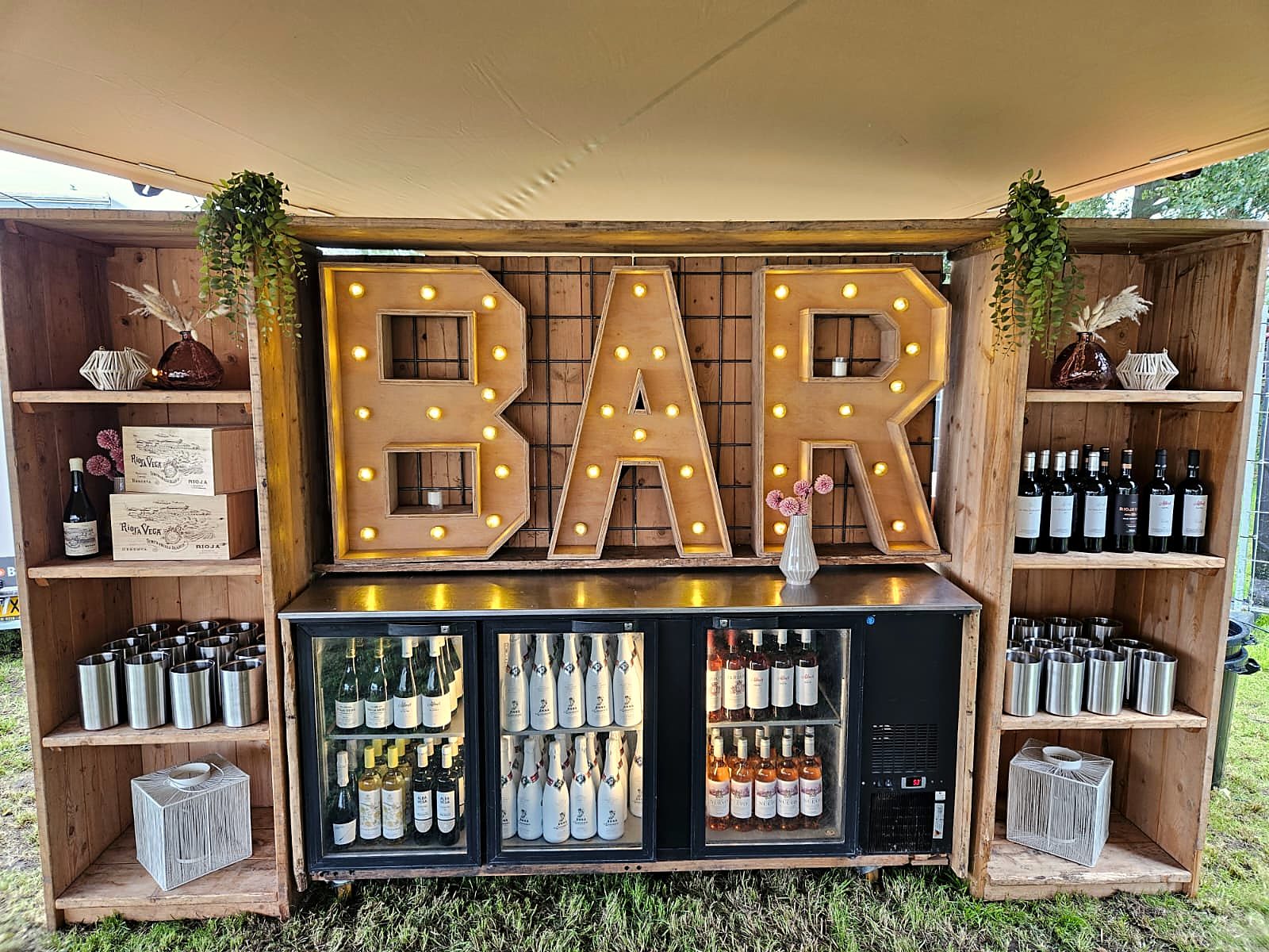 De bar: verlichte letters BAR, houten kasten en een koelkast vol flessen