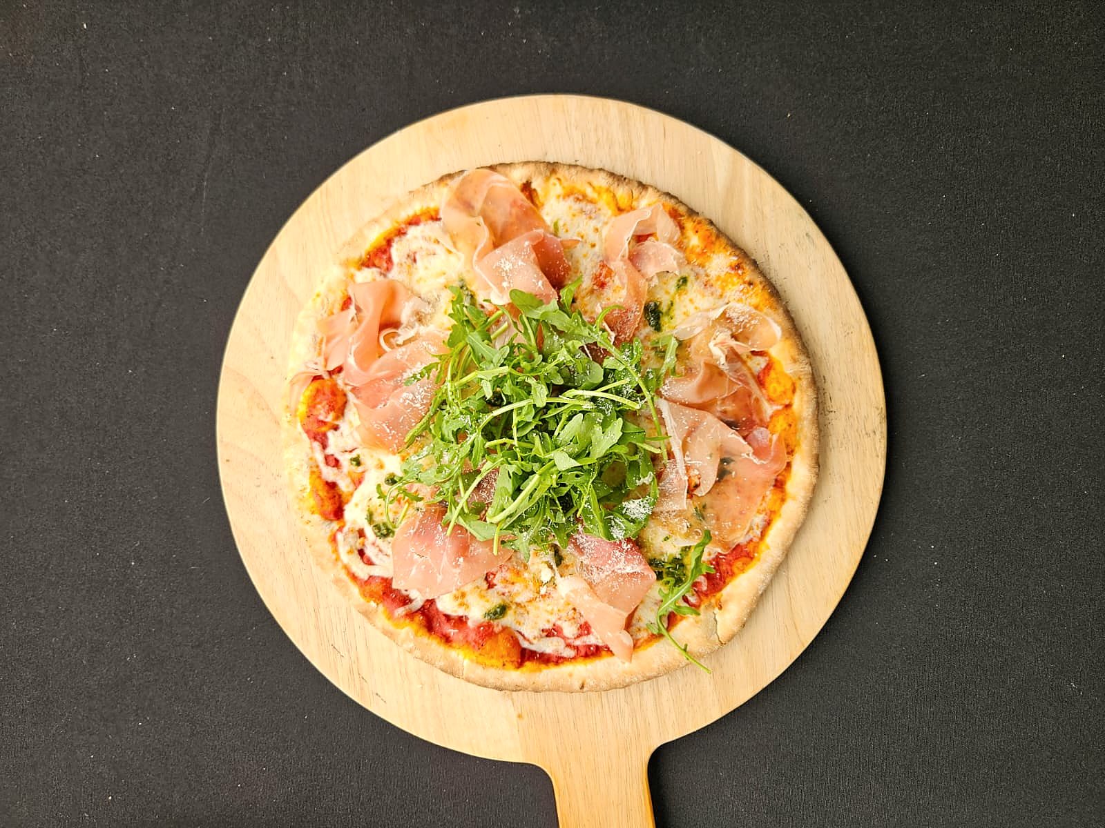 Pizza met rauwe ham en rucola op een houten plank